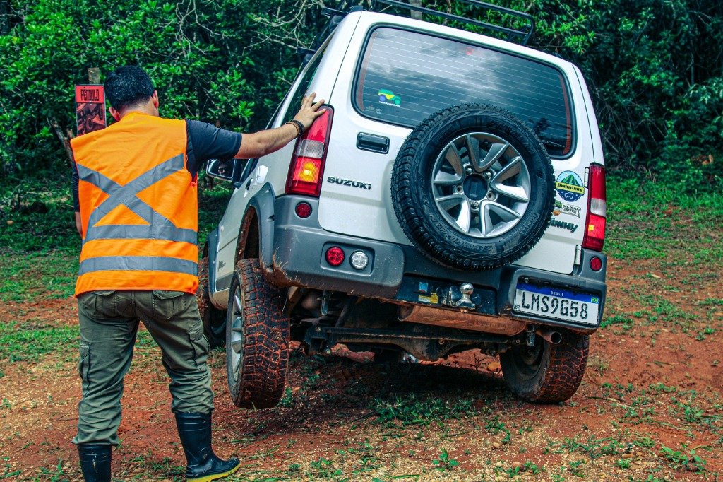 Suzuki Jimny no obstáculo do pêndulo com a roda traseira totalmente no ar e o instrutor orientando